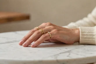 Femme portant plusieurs bagues en or sur différents doigts, posées sur une surface en marbre, illustrant la signification des bagues selon les doigts