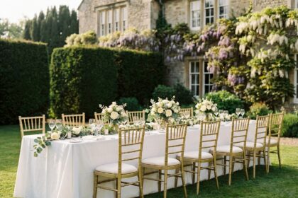 Chaises Chiavari dorées avec coussins ivoire disposées autour d'une longue table de réception de mariage en extérieur dans un jardin élégant